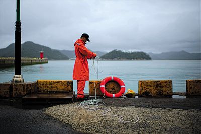 7月6日，韓國(guó)珍島，一名海岸警察在港口系救生圈。4月，客輪在珍島近海發(fā)生沉船事故后，仍有11人下落不明。