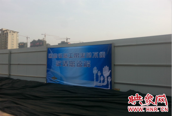 道路南側(cè)圍起了白色的圍擋，墻上標示著“因地鐵施工帶來的不便敬請您諒解”的提示牌。