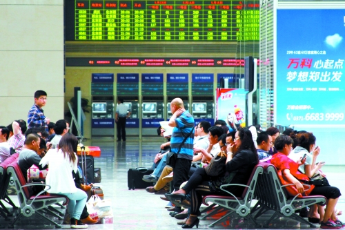 候車大廳溫度很高，一名乘客一手扇風(fēng)、一手擦汗