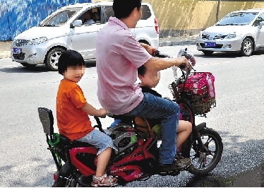 周先生騎著一輛低矮的電動車帶著一對兒女，很不安全。