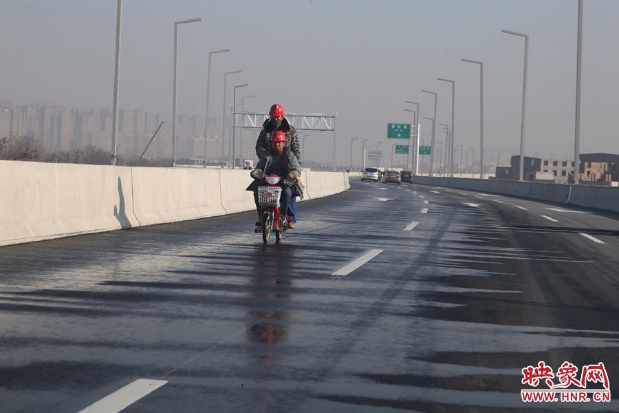 兩名工人騎車經(jīng)過灑水養(yǎng)護路面。